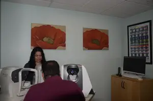 A man is getting his eyes checked by an eye doctor in a room with paintings on the wall