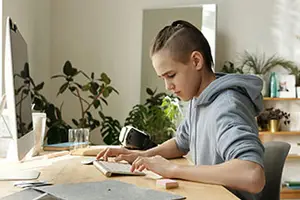 A young boy is typing on a keyboard in front of a computer monitor.