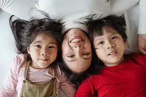 Three young children are lying down on a bed, smiling and posing for a photograph.