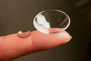 A fingertip with a clear contact lens resting on it against a dark background.