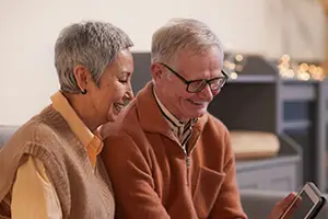 Two older people sitting on a couch looking at a tablet smiling