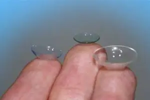 Two clear contact lenses are held between the fingers of a person.