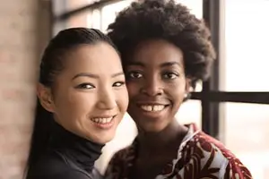 Two women, one Asian and one African American, are standing next to each other and smiling at the camera.