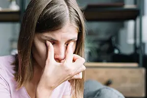 A woman is sitting down with her hands on her face looking sad