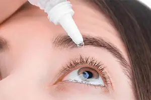 A woman is applying eye drops near her eyebrow, focusing on her eye.