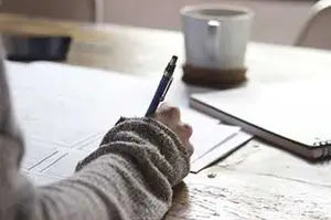 A person is writing on a paper with a pen on a wooden table
