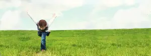 A young boy doing a cartwheel in a grassy field under a cloudy sky