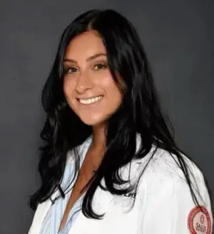 a woman with long black hair wearing a white lab coat and smiling for the camera