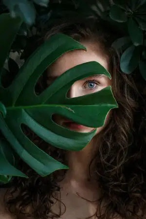 Woman peeking out from behind a large green leaf