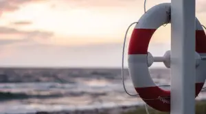 A lifebuoy is attached to a pole by a wire and is positioned against the backdrop of a tranquil ocean at sunset.