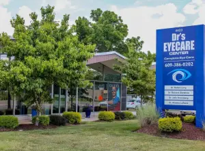 Dr's Eyecare Center's entrance has a blue sign with a logo, a picture of a man in a blue shirt, and a phone number.
