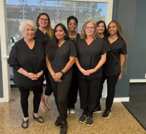 Seven women in black outfits pose for a photograph in an office.