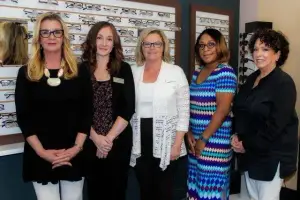 Five women standing in front of a display of eyeglasses in a store