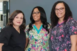 Three women standing together in a medical facility with smiles on their faces
