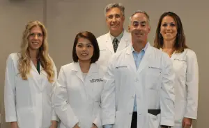 Six medical professionals stand in a row in white coats for a group photo