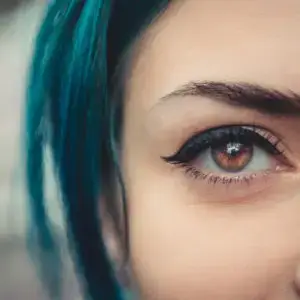 Close-up of a woman with blue hair and brown eyes with eyeliner and mascara on.