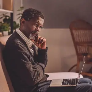 A man sitting on a couch with a laptop on his lap and a chair behind him