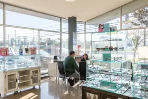 Two people are sitting in chairs in front of a glass cabinet with glasses in an optical shop.