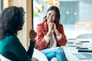 Two women sitting at a table and having a conversation, one smiling and the other listening attentively