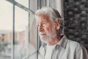 Elderly man looking out of window with sad expression