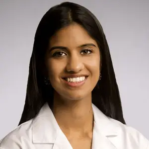 Close-up portrait of a smiling female doctor with long black hair wearing a white coat