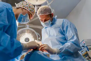 Two doctors in blue scrubs perform surgery in a well-lit operating room.