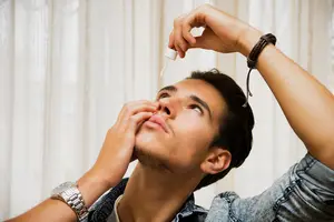 A man drops eye drops into his eye.