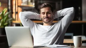 Man sitting at a desk in an office setting with a laptop and coffee mug