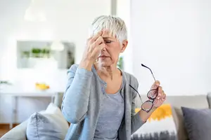 Senior woman rubs her eyes while feeling the symptoms of Meibomian Gland Dysfunction