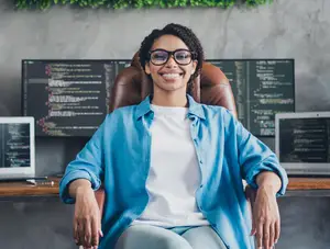 Woman wearing glasses and smiling in front of computer monitors