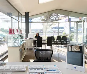 An adult female sitting in front of a desk with a computer in an office room with glass walls and chairs.