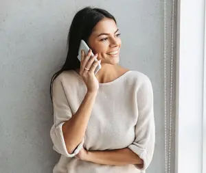 A woman in a white sweater talking on her phone with a smile on her face