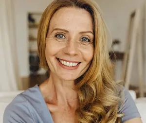 A woman with blonde hair and a blue shirt smiling at the camera in a room