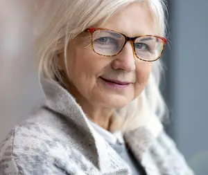 portrait of a happy elderly woman wearing glasses and a gray coat smiling at the camera