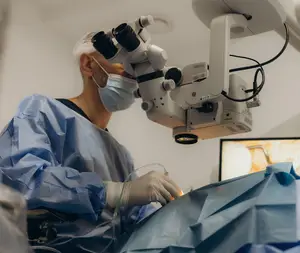 A medical professional performing surgery with surgical tools and an operating microscope.