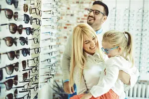 A family is looking at sunglasses in a store with a brick wall in the background.