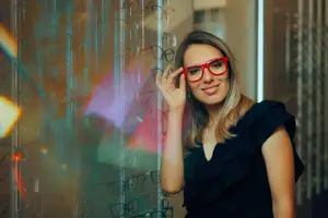 Woman wearing red glasses standing in front of a glass wall with a reflection of an indoor area