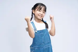 Happy young girl wearing blue overalls with her fists up