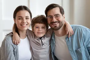 A family of three, a woman, a man, and a boy, standing close to each other in a room, smiling and posing for a photo