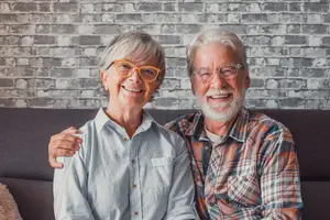 Elderly couple smiling and sitting on a couch in front of a brick wall