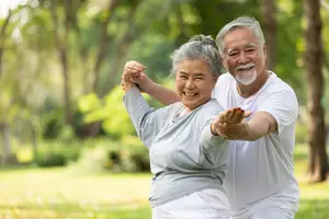An elderly couple dancing in a park with trees and grass in the background