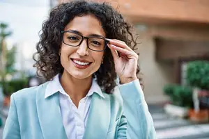 A woman is smiling while adjusting her glasses on the street.