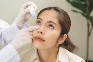 A doctor administering eye drops to a woman sitting in a chair