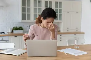 woman sitting at a desk in the kitchen rubbing her eyes