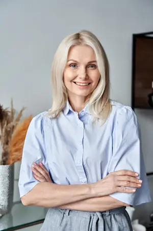 A woman with blonde hair is smiling and posing for a photo while standing in front of a glass table