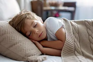 A boy sleeping on a bed with a beige blanket