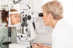 An optometrist checks a young girl's eye with a machine