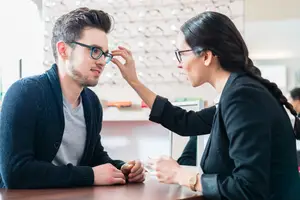 Man getting his glasses adjusted by a woman in a business suit.