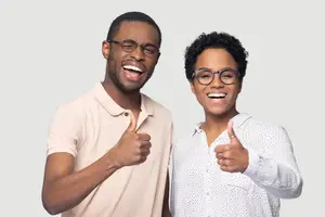 Two men standing next to each other, smiling and giving a thumbs up sign