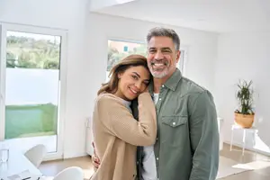 A smiling couple in a white living room with a table and chairs